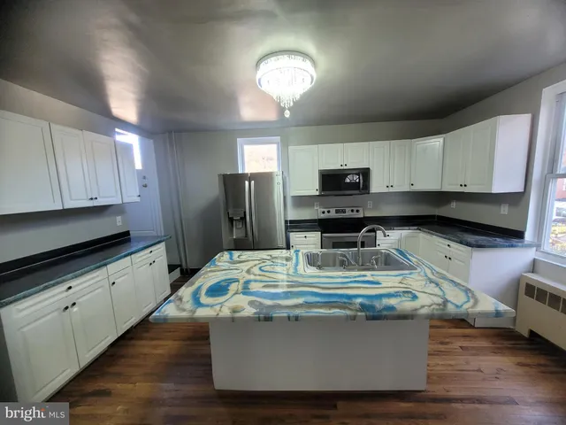 a kitchen with kitchen island granite countertop a stove a sink a refrigerator and white cabinets