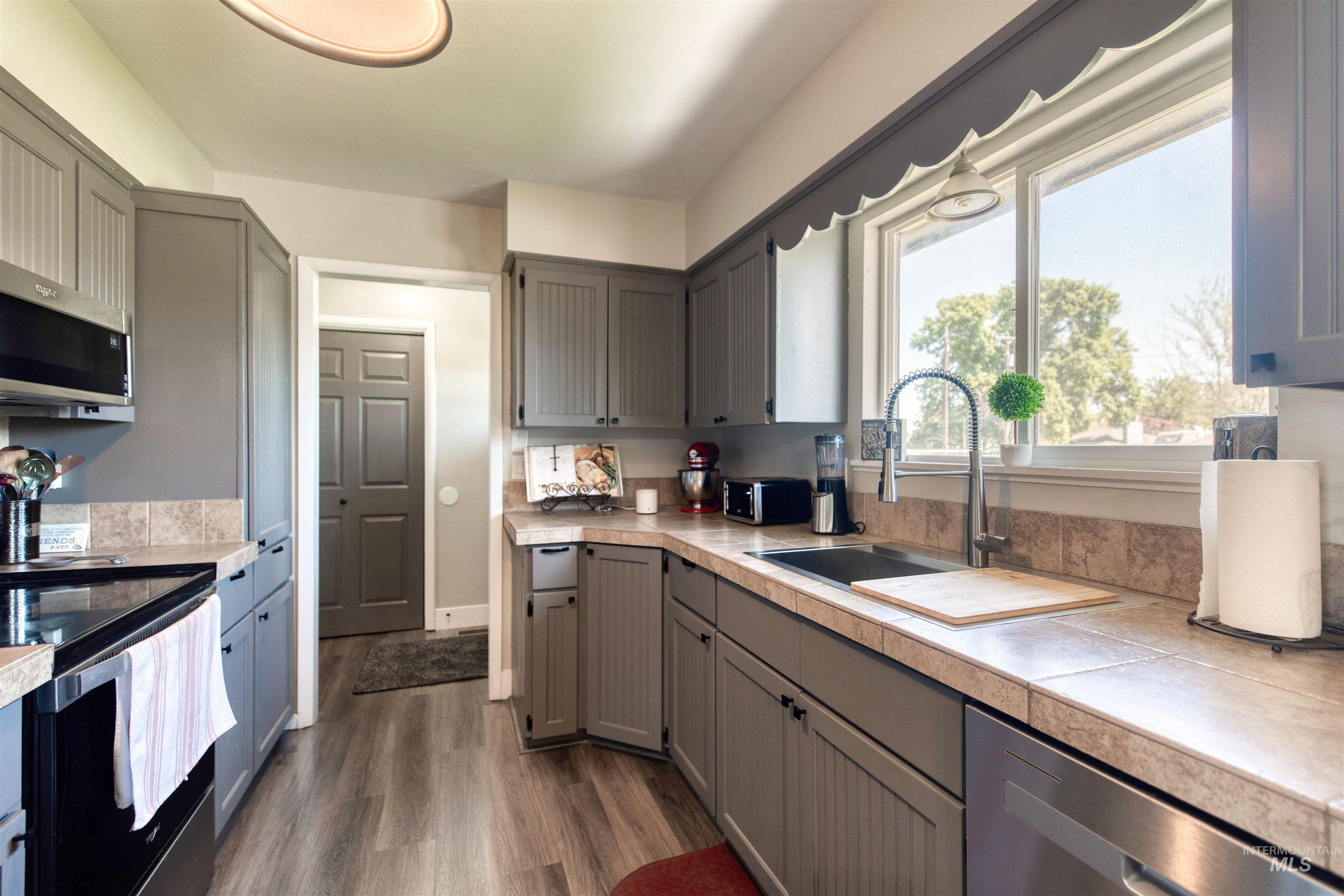 20803 Friends Road Greenleaf, ID 83626 - Photo 7 of 39 Galley-style kitchen featuring wood-finish flooring, gray shaker-style cabinetry with black hardware, a tile countertop, and a stainless steel sink with a high-arch faucet
