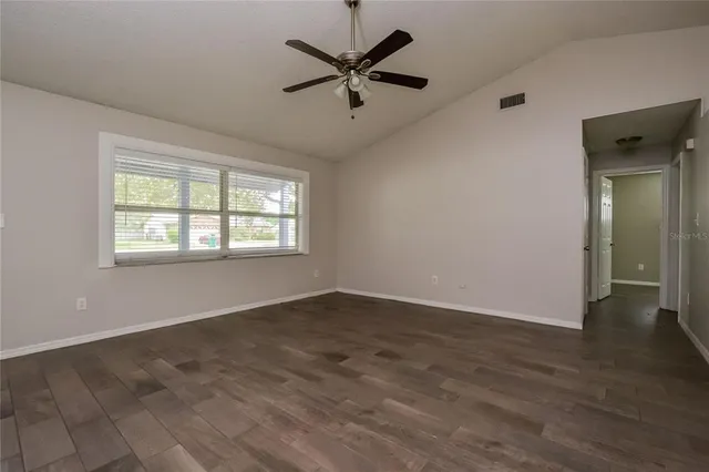 an empty room with wooden floor chandelier fan and windows