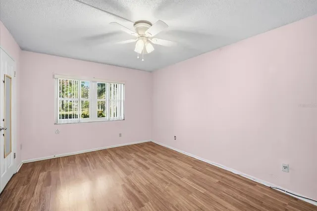 an empty room with wooden floor chandelier fan and windows
