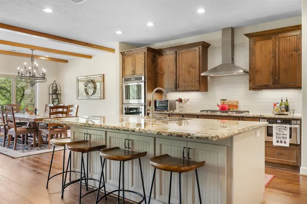 a kitchen with stainless steel appliances granite countertop a stove top oven a sink a refrigerator and chairs