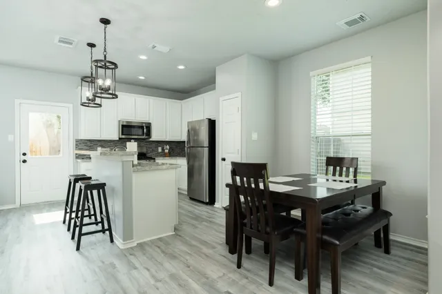 a room with stainless steel appliances kitchen island granite countertop a dining table chairs and a refrigerator