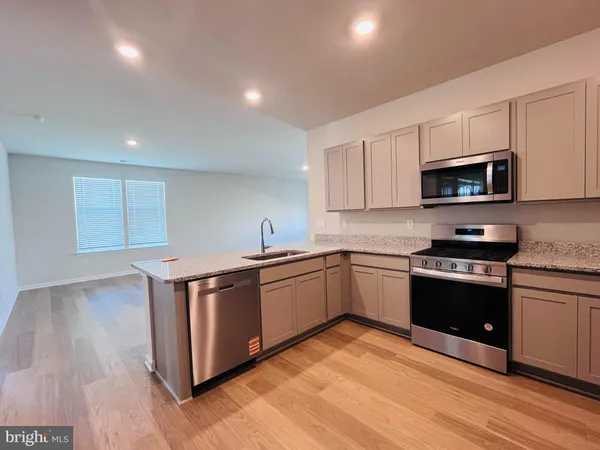 a kitchen with stainless steel appliances granite countertop a stove top oven a sink dishwasher and a microwave oven with wooden floor