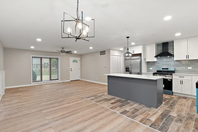 a kitchen with stainless steel appliances granite countertop a refrigerator a sink dishwasher a stove and white cabinets with wooden floor