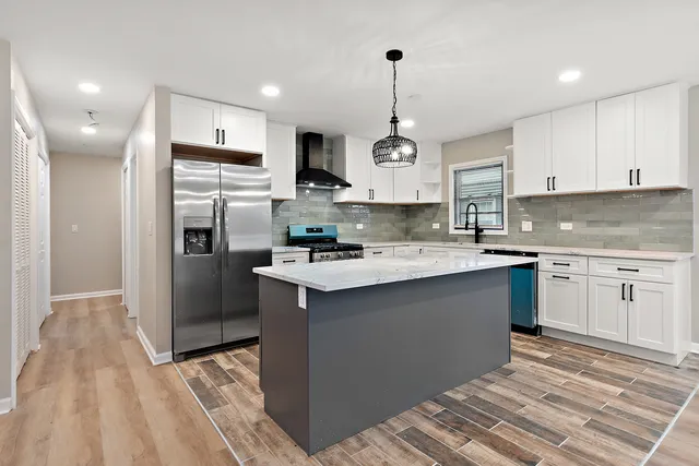 a kitchen with stainless steel appliances kitchen island granite countertop a refrigerator a sink dishwasher a stove and white cabinets with wooden floor