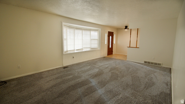 2455 South Bluff Road Syracuse, UT 84075 - Photo 9 of 32 Spacious room featuring gray carpeting, a bay window with white blinds, a wood-paneled entry door, and a ceiling fan