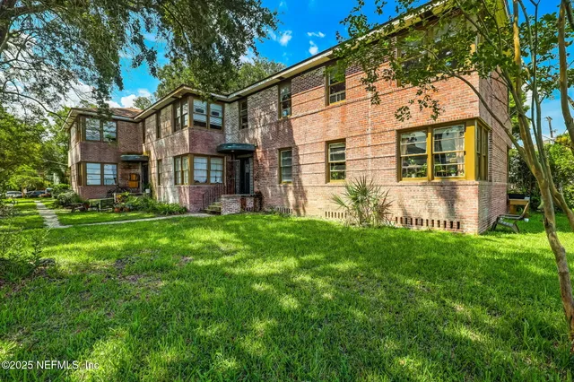 a view of a yard in front of a brick house with a large tree
