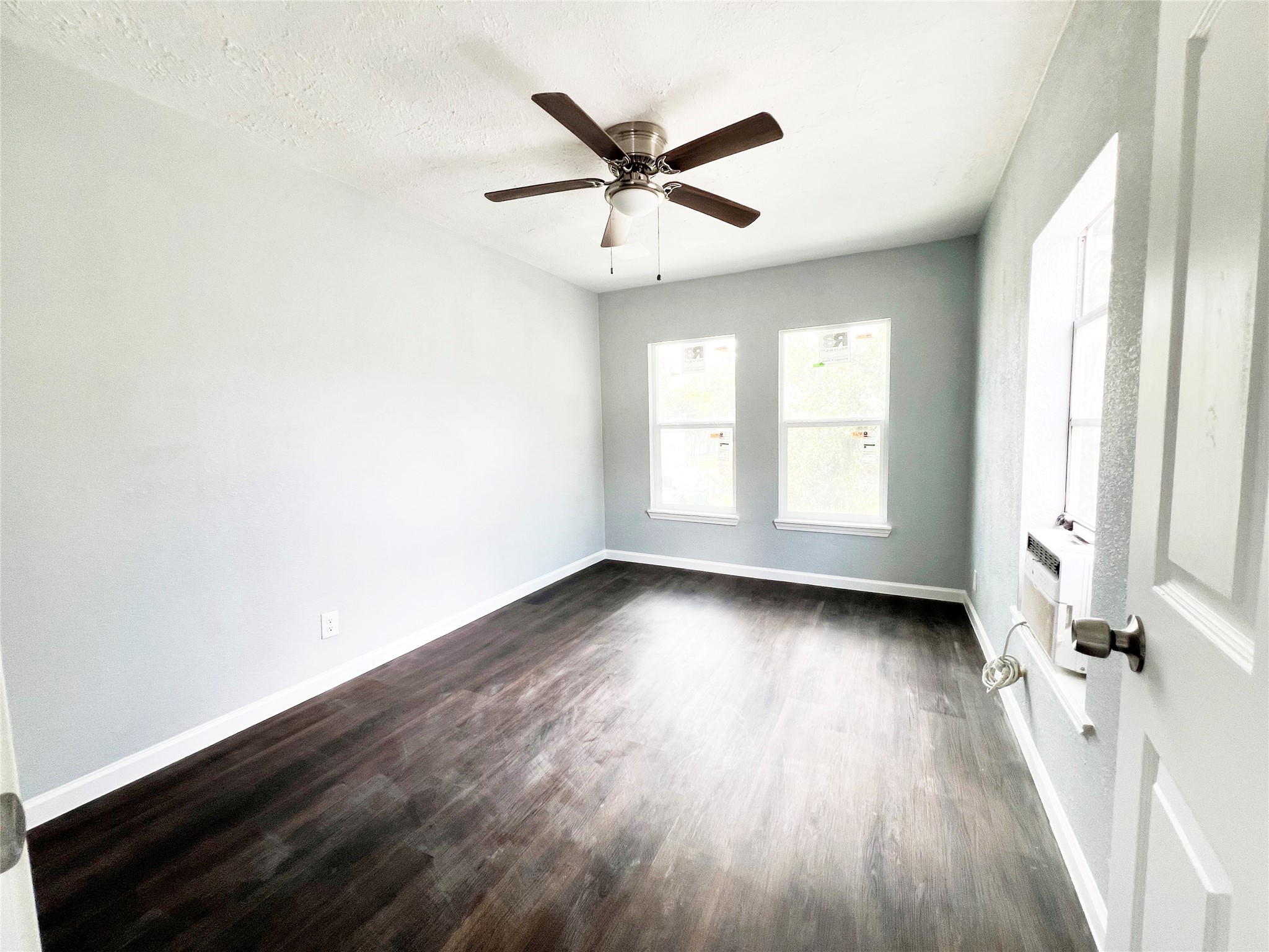 an empty room with wooden floor fan and windows