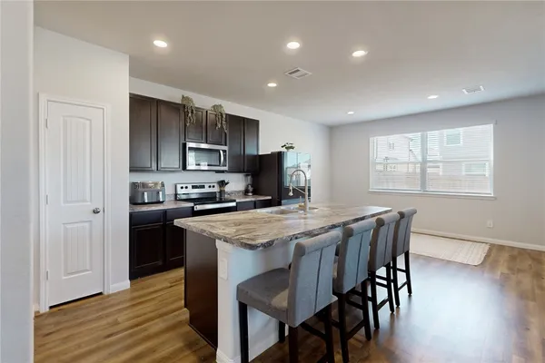 a kitchen with stainless steel appliances granite countertop a stove a refrigerator a sink dishwasher a dining table and chairs with wooden floor