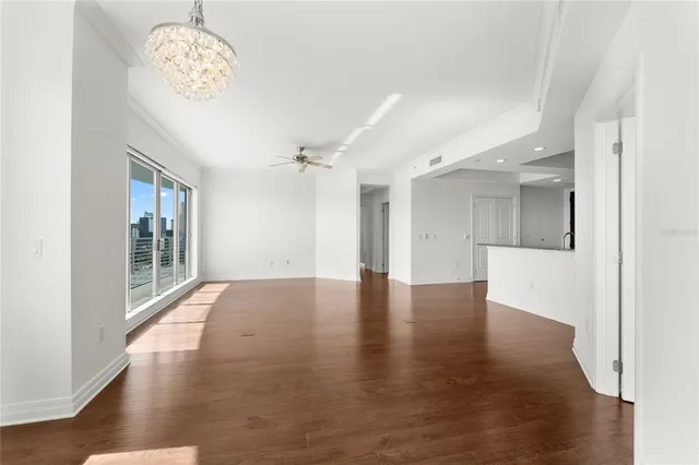 a view of an empty room with wooden floor and a kitchen