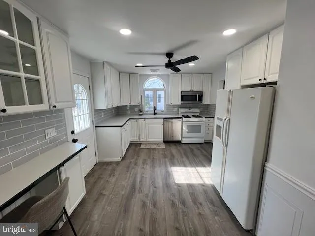 a kitchen with granite countertop a refrigerator a sink dishwasher a stove and white cabinets with wooden floor