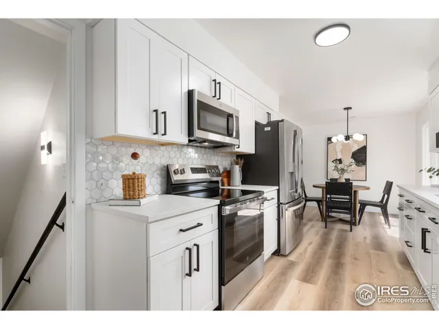 a kitchen with stainless steel appliances granite countertop a stove top oven a refrigerator a sink dishwasher and white cabinets with wooden floor