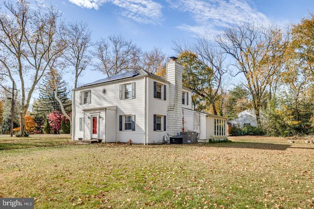 a view of a white house with a yard covered with large trees