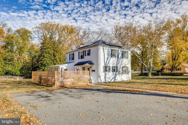 a view of a white house next to a yard with large trees