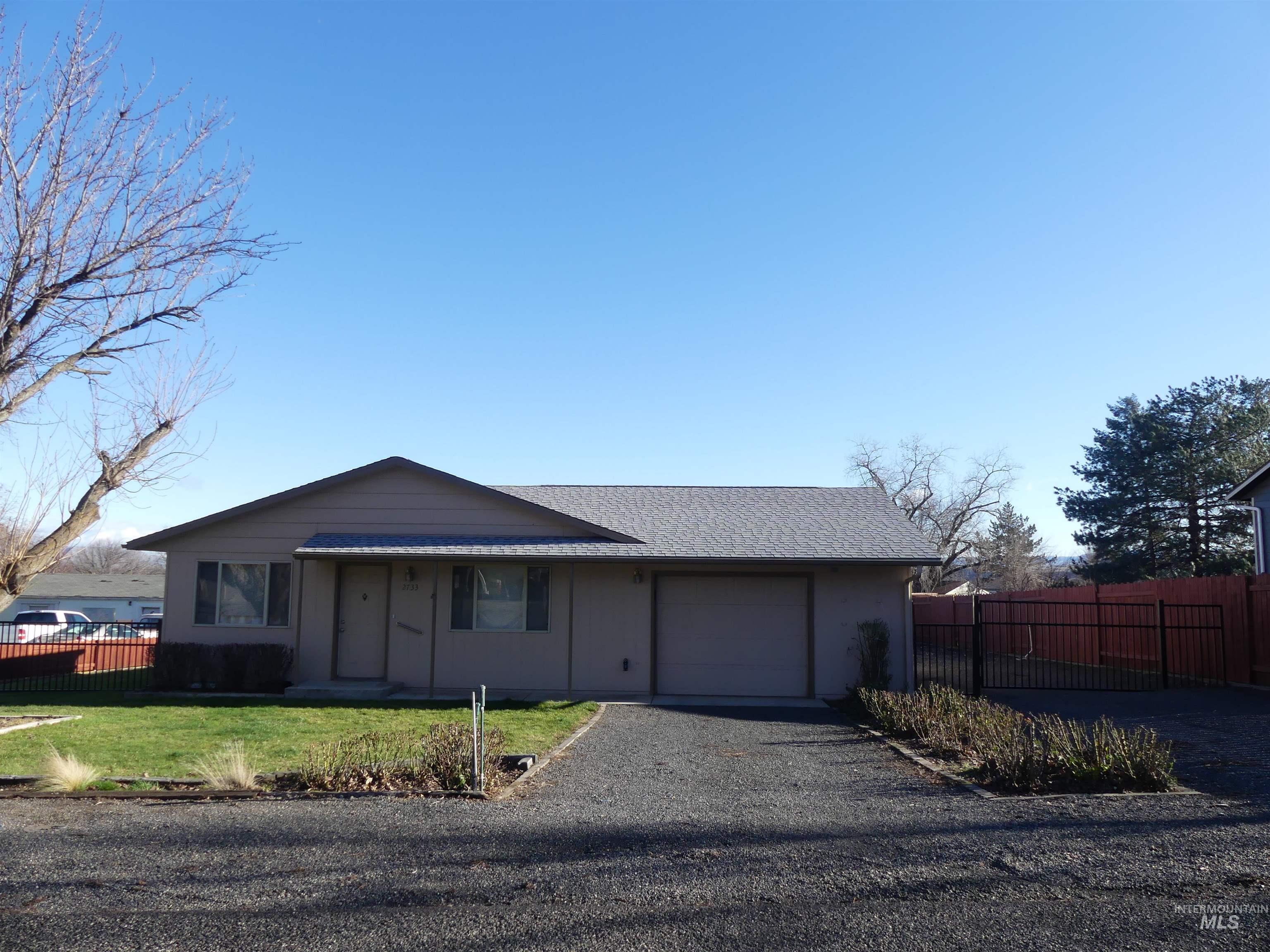 View of front of home featuring gravel driveway, an attached garage, and a shingled roof