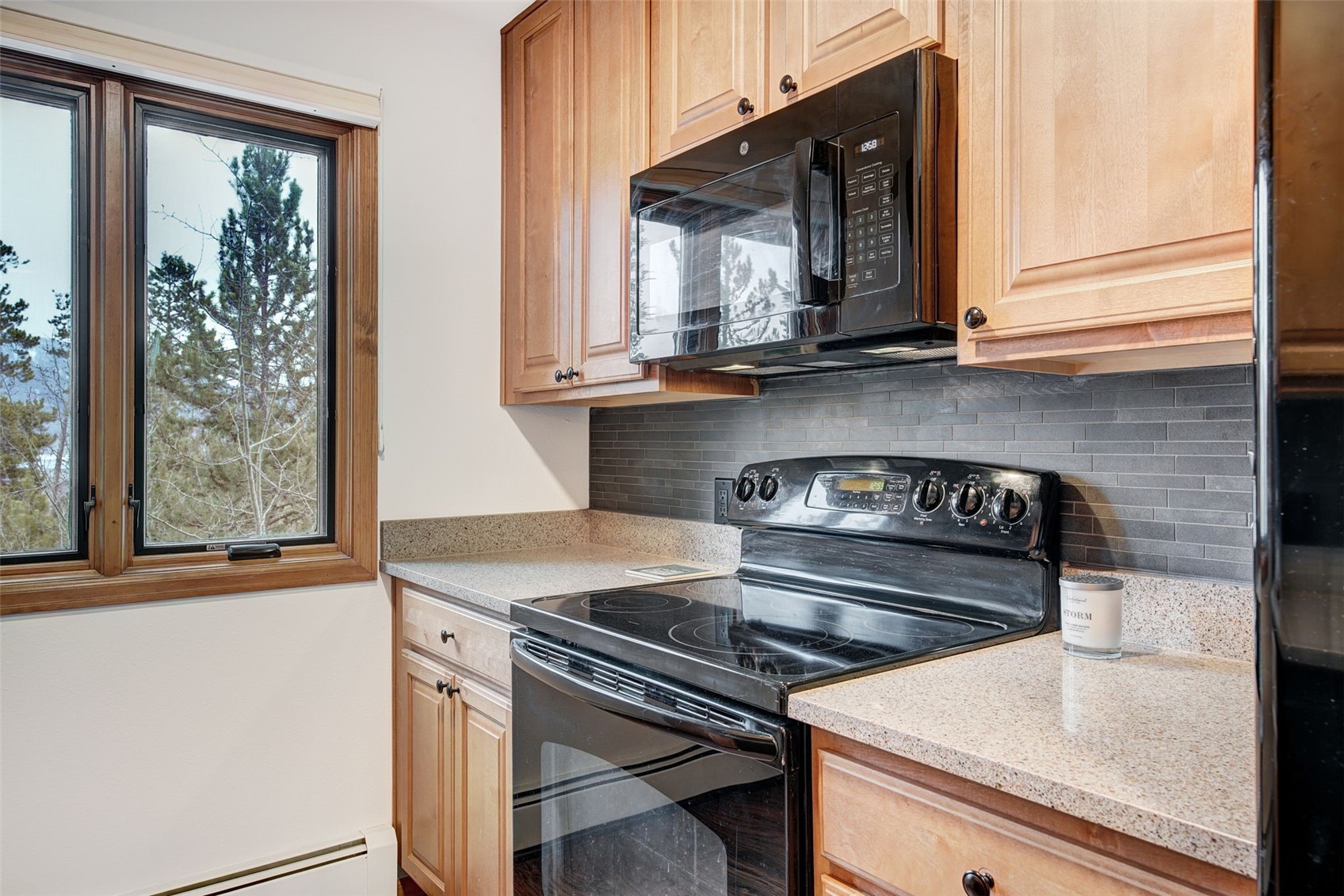 3710 Ryan Gulch Road, Unit 378 Silverthorne, CO 80498 - Photo 12 of 31 Kitchen featuring black appliances, light stone counters, a baseboard radiator, backsplash, and light wood finish cabinets