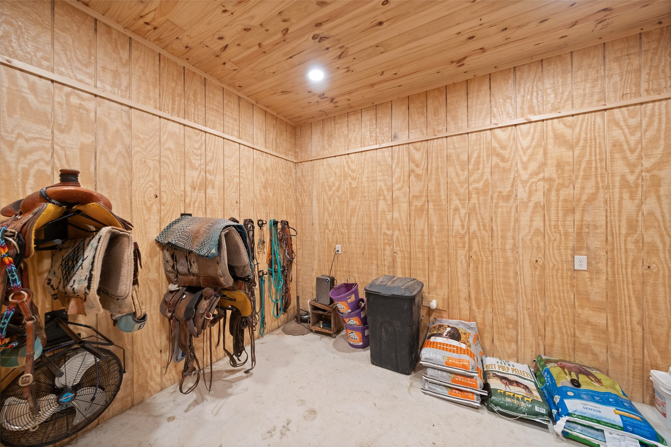 1402 Eagle Ferry Road Anahuac, TX 77514 - Photo 9 of 48 Finished with wood paneling and equipped with saddle racks, bridle hooks, and feed storage, this insulated tack room keeps equipment organized, secure, and protected in all seasons.