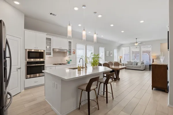 a kitchen with stainless steel appliances kitchen island granite countertop a refrigerator a stove a sink a dining table and chairs with wooden floor