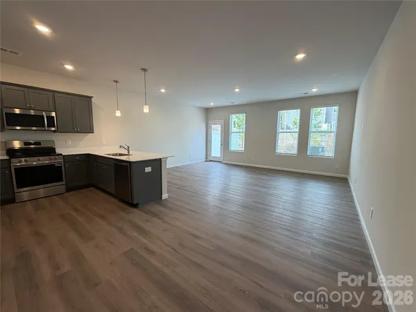 a large kitchen with stainless steel appliances granite countertop a large counter top a wooden floors and a view of living room