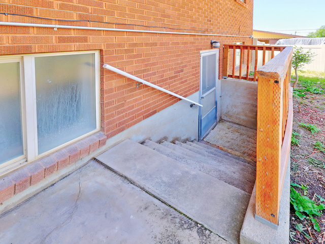 1272 Cook Street Ogden, UT 84404 - Photo 5 of 58 Concrete stairs descending to a basement entry, featuring a screen door and an overhead exterior light