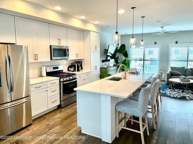 a kitchen with stainless steel appliances kitchen island granite countertop a refrigerator a stove a sink a dining table and chairs with wooden floor