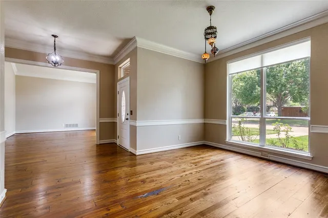 an empty room with wooden floor chandelier and windows