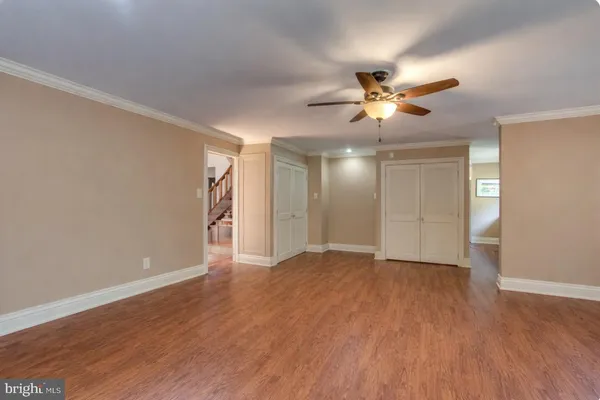 a view of an empty room with wooden floor and a ceiling fan