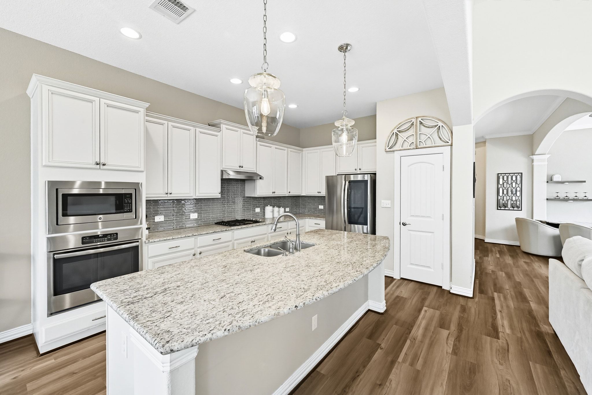 19620 Stanton Drew Pflugerville, TX 78660 - Photo 10 of 33 Kitchen with arched walkways, stainless steel appliances, white cabinetry, pendant lighting, and a center island with sink