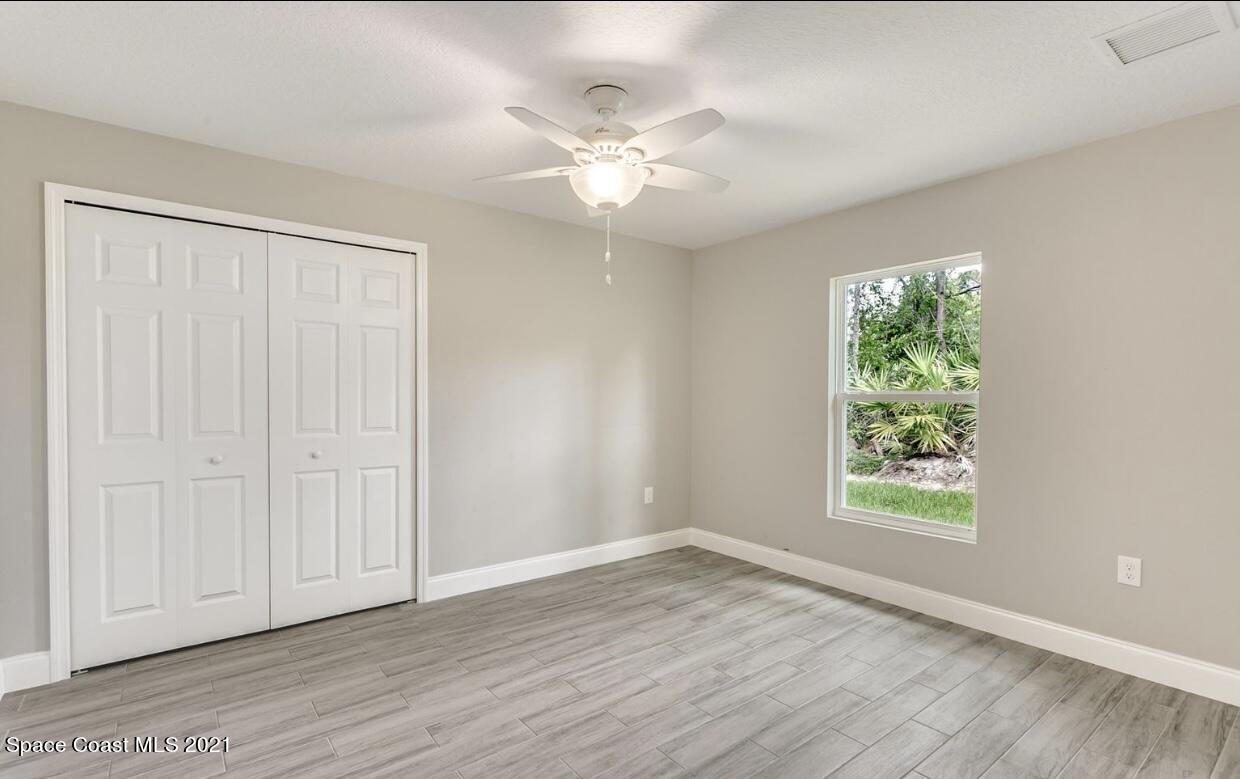 1738 Hydrangea Road Palm Bay, FL 32907 - Photo 7 of 20 an empty room with wooden floor chandelier fan and windows