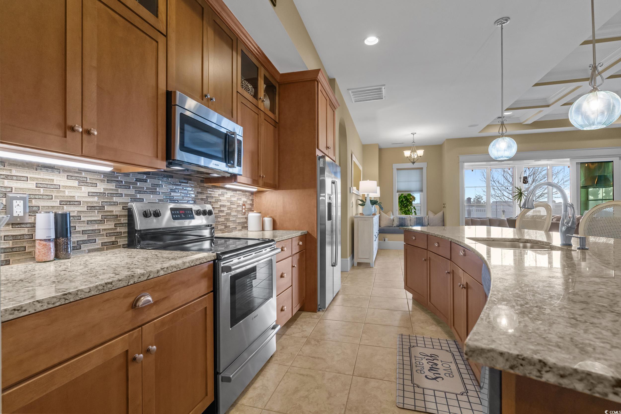 2604 Painted Trillium Court Myrtle Beach, SC 29579 - Photo 9 of 40 Kitchen with appliances with stainless steel finishes, light stone counters, brown cabinetry, glass insert cabinets, and backsplash