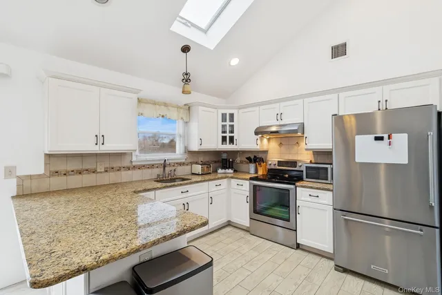 a kitchen with granite countertop a refrigerator oven a sink and white cabinets