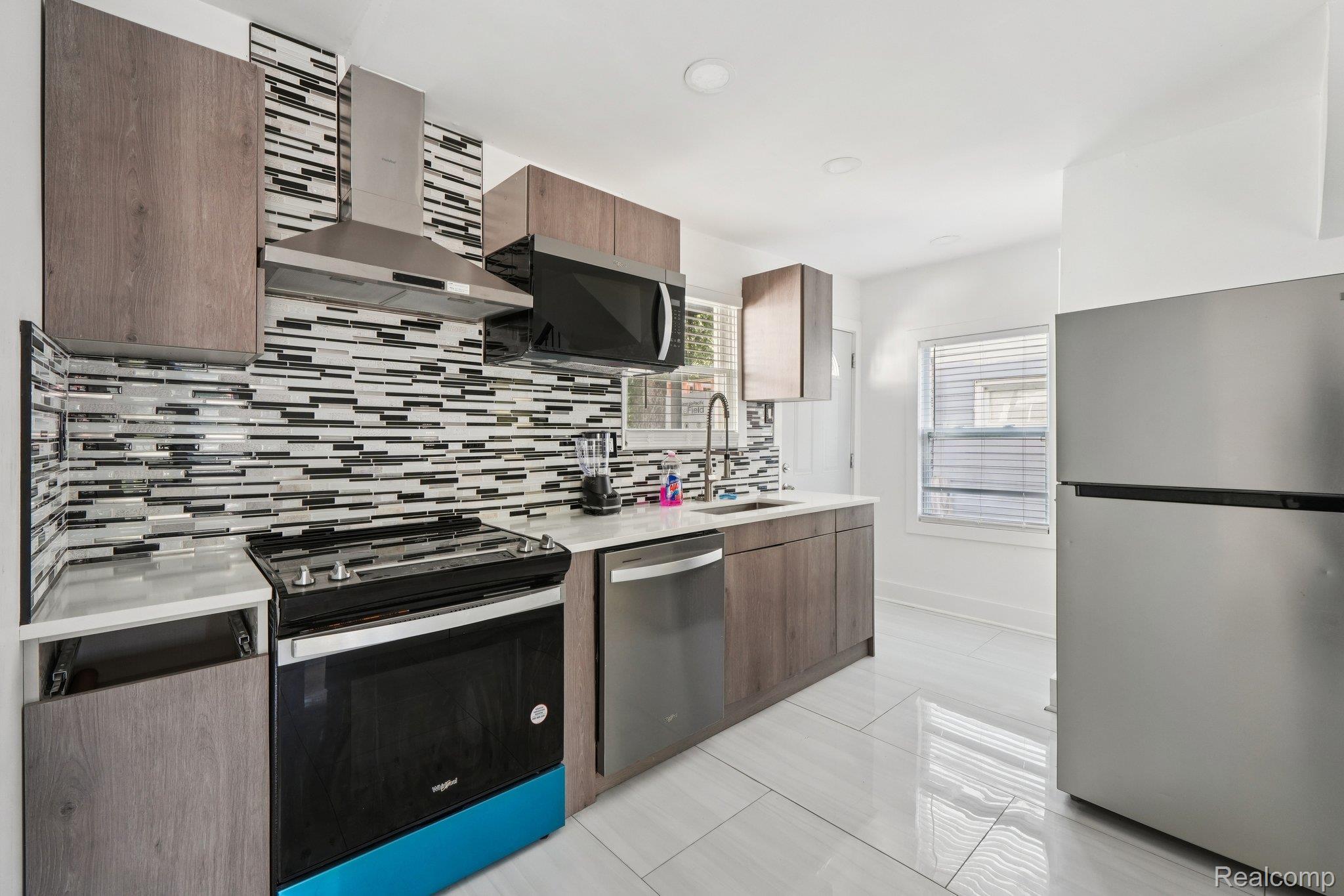 16210 Inverness Street Detroit, MI 48221 - Photo 10 of 29 Modern kitchen featuring wood-finish cabinetry, stainless steel appliances, a mosaic tile backsplash, white countertops, and sleek tile flooring