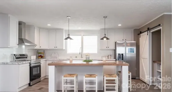 a kitchen with stainless steel appliances granite countertop a refrigerator a sink dishwasher a stove and white cabinets with wooden floor