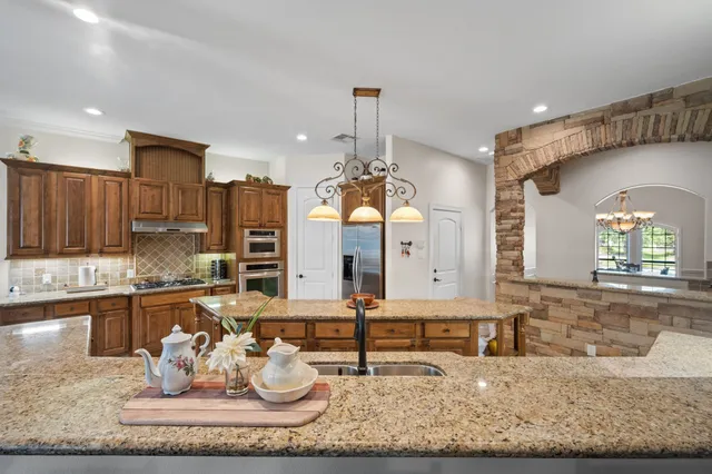 a kitchen with kitchen island granite countertop cabinets a sink and a chandelier