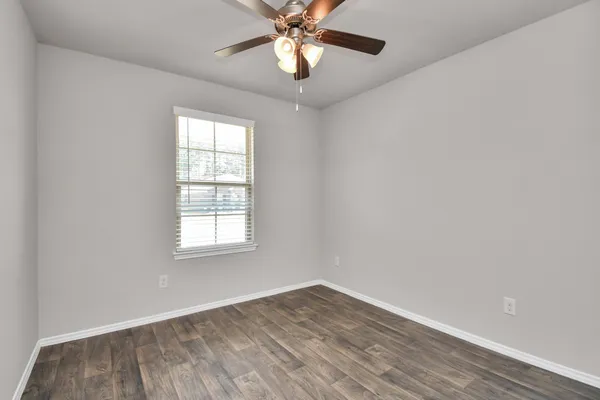 an empty room with wooden floor fan and windows