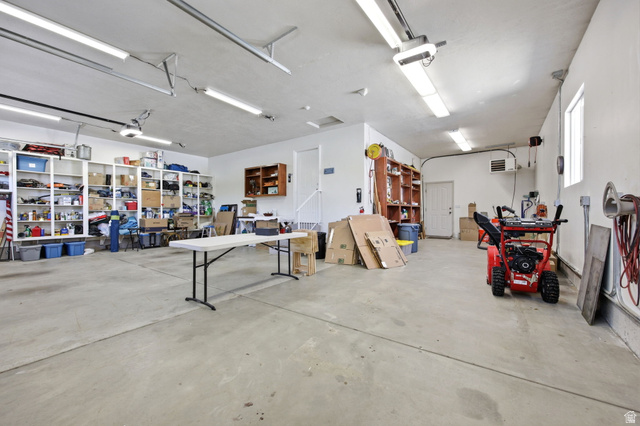 776 Flint Street Layton, UT 84041 - Photo 35 of 41 Spacious garage featuring a concrete floor, built-in shelving, ample overhead lighting, multiple windows, and a dedicated utility door