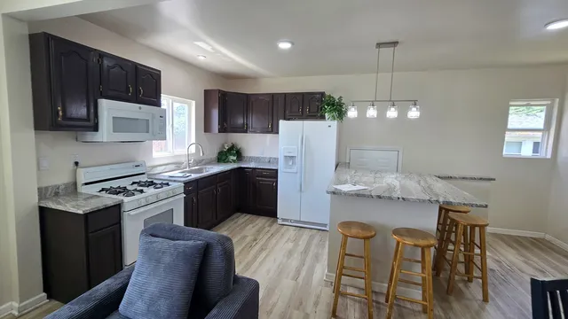 a kitchen with stainless steel appliances granite countertop a refrigerator a stove a sink dishwasher a dining table and chairs with wooden floor