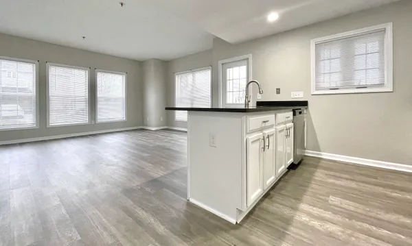 a kitchen with stainless steel appliances granite countertop a stove a sink and white cabinets with wooden floor next to windows