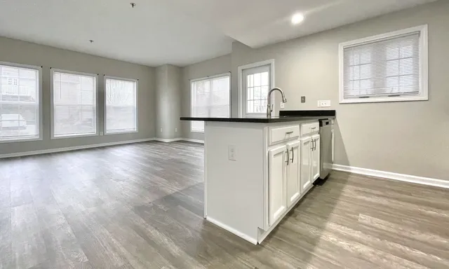 a kitchen with stainless steel appliances granite countertop a stove a sink and white cabinets with wooden floor next to windows