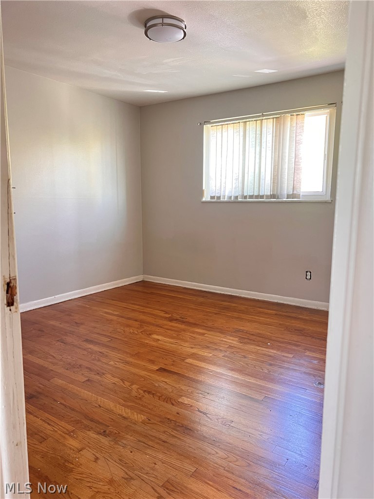 16350 Rockside Road Maple Heights, OH 44137 - Photo 22 of 34 Room featuring wood-finish flooring, a window with vertical blinds, a flush-mount ceiling light fixture, and white baseboards