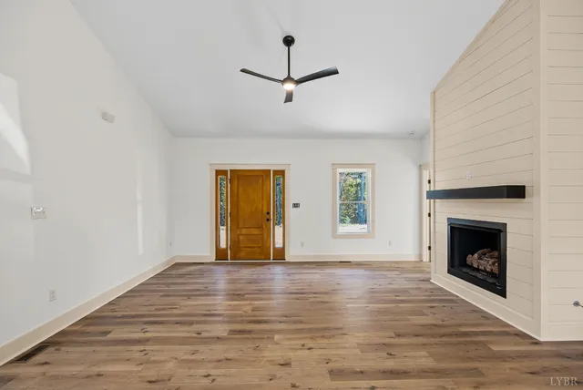 a view of an empty room with wooden floor fireplace and a window