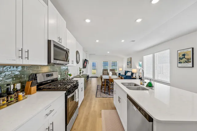 a large kitchen with stainless steel appliances a stove a sink a oven a dining table and chairs with wooden floor