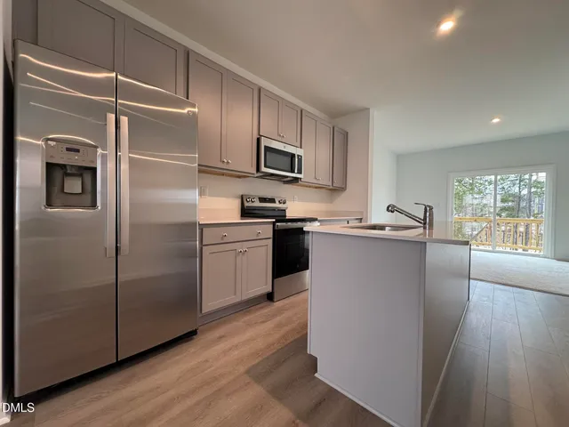a kitchen with stainless steel appliances granite countertop a refrigerator a sink a stove top oven a refrigerator with grey cabinets and wooden floor