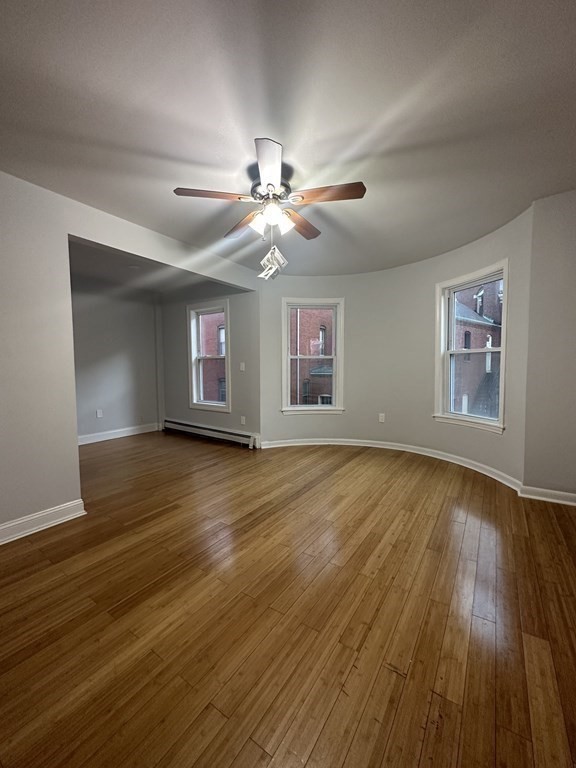a view of a livingroom with wooden floor a ceiling fan and windows