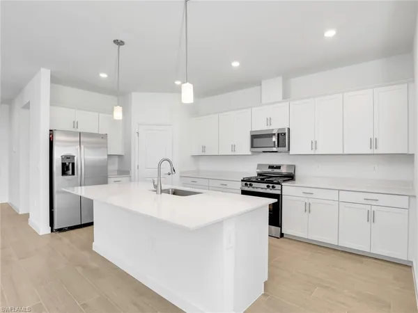 a kitchen with stainless steel appliances granite countertop a sink a stove a refrigerator and white cabinets with wooden floor
