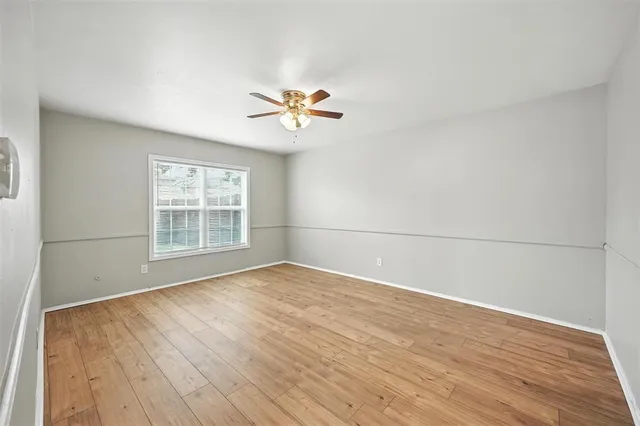 an empty room with wooden floor fan and windows