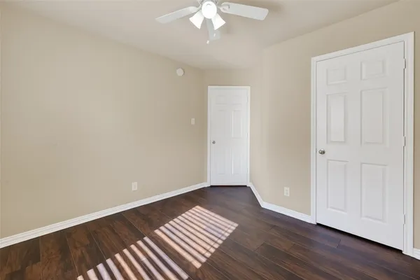 a view of an empty room with wooden floor and a ceiling fan