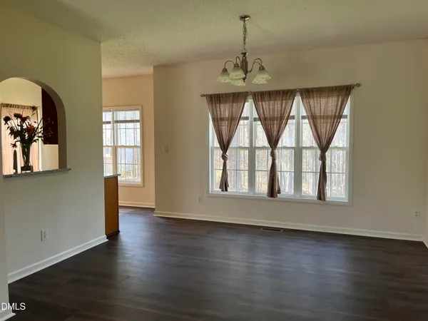an empty room with wooden floor chandelier and windows