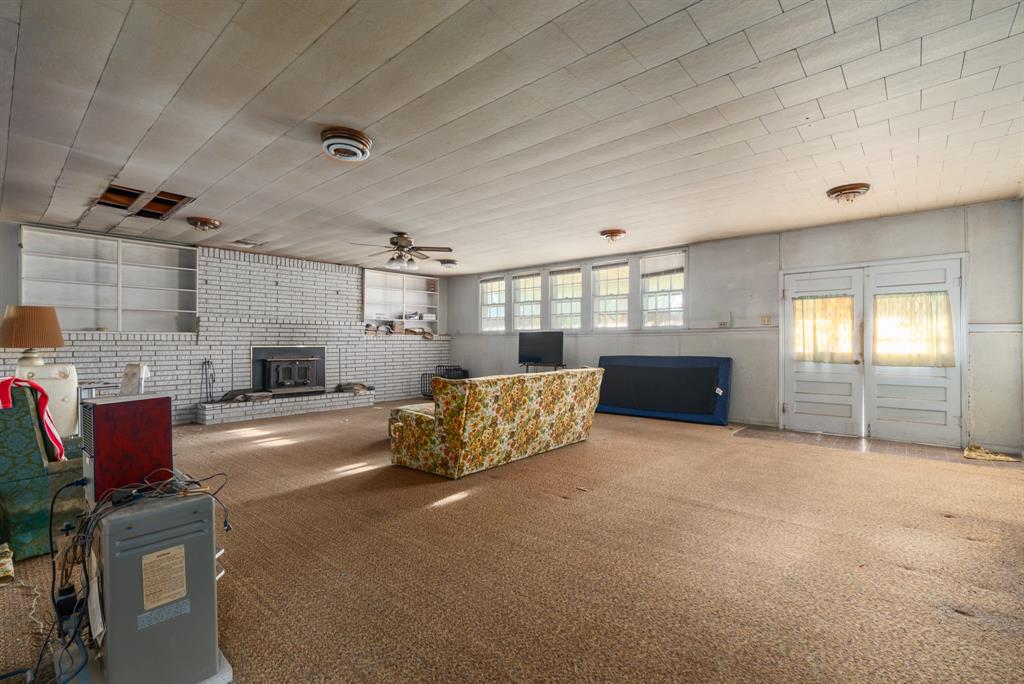 1089 Highway 22 Whitney, TX 76692 - Photo 5 of 26 Carpeted living room with brick wall, a ceiling fan, and a wood stove