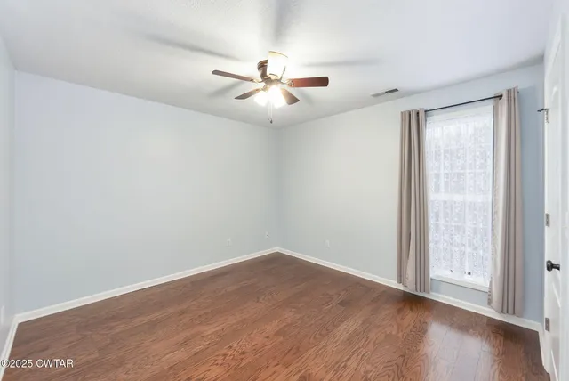 an empty room with wooden floor fan and windows